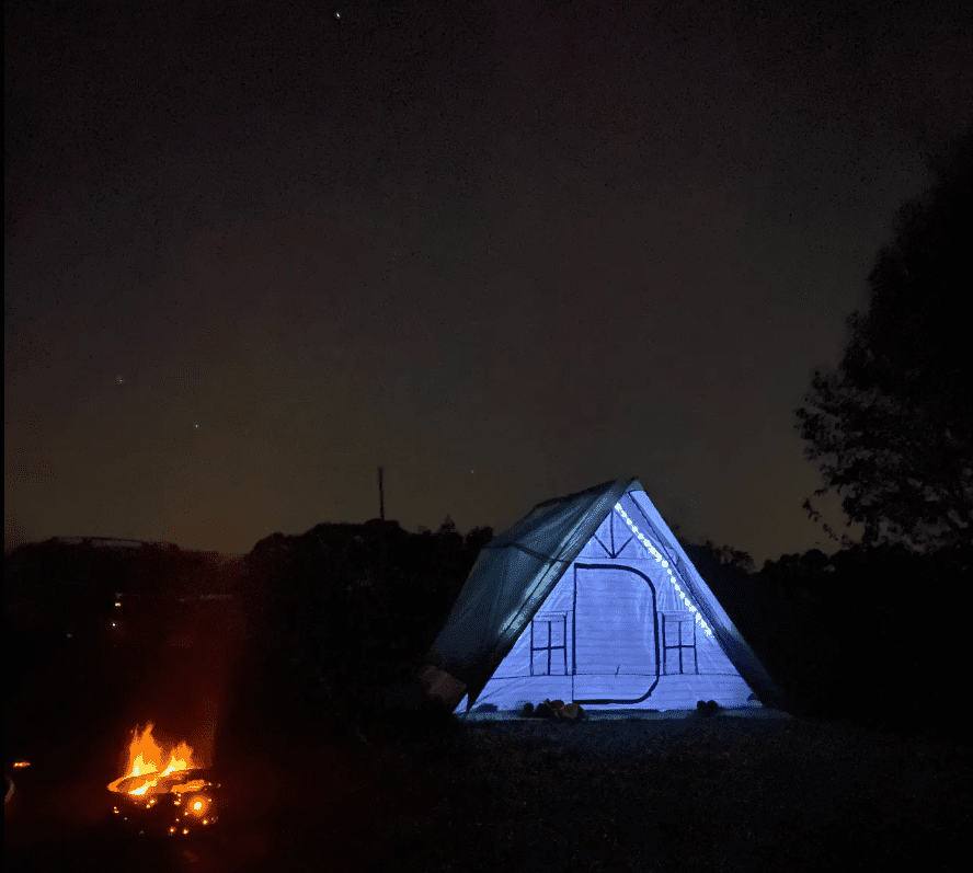 image of an illuminated tent pitched next to a campfire under a night sky full of stars